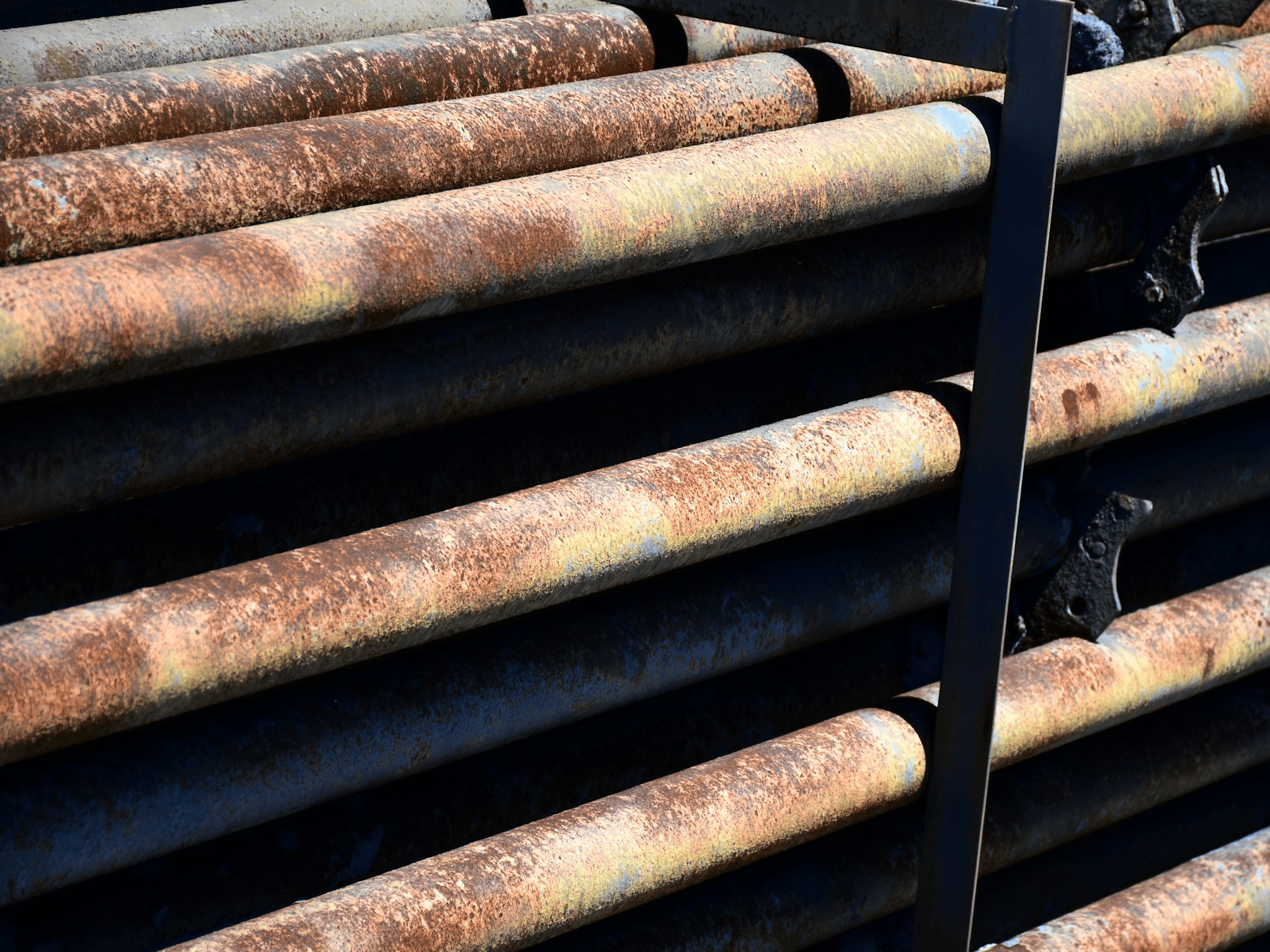 Une pile de tuyaux métalliques rouillés, alignés horizontalement, avec une coloration brun-orange sur leur surface indiquant la corrosion.